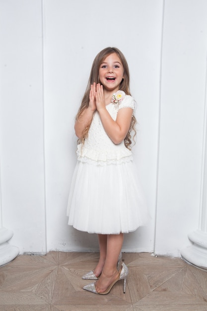 Foto animada e emocional linda garota com vestido branco da moda se divertindo e usando mães grandes e saltos altos brilhantes