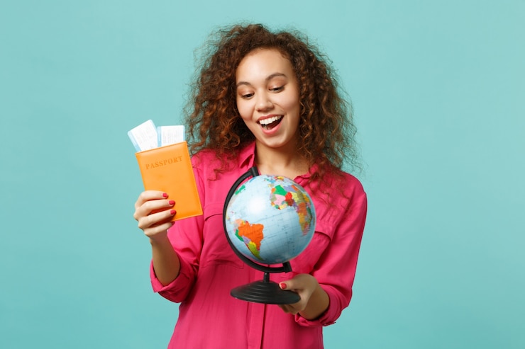 Foto animada garota africana em roupas casuais, segurando o globo do mundo terra, passaporte, bilhete do cartão de embarque, isolado no fundo azul turquesa. emoções sinceras de pessoas, conceito de estilo de vida. simule o espaço da cópia.