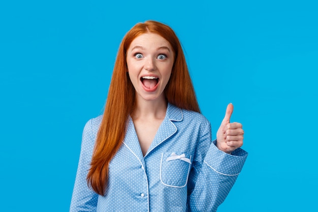 Animada, impressionada e oprimida, jovem e bonita mulher ruiva de pijama, gritando de emoção e espanto, encontrou exatamente o que estava procurando mostrar polegares para cima em aprovação, curtida ou recomendação