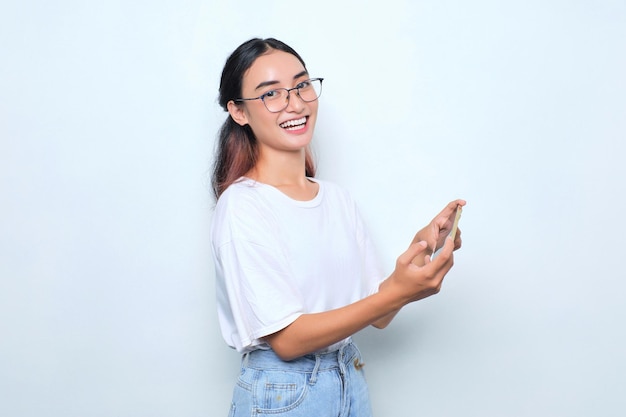 Animada jovem asiática em camiseta branca jogando jogo no celular isolado em fundo branco