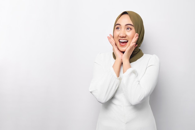 Animada jovem muçulmana asiática de 20 anos usando hijab olhando para o espaço da cópia e levantando as mãos com a boca aberta reagindo à oferta de venda isolada no fundo branco Conceito de estilo de vida religioso de pessoas