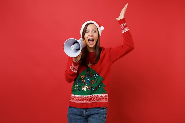 Animada jovem santa no chapéu de natal subindo, espalhando as mãos, gritando no megafone isolado em fundo vermelho brilhante. conceito de festa de feriado de celebração de ano novo feliz 2019. simule o espaço da cópia.