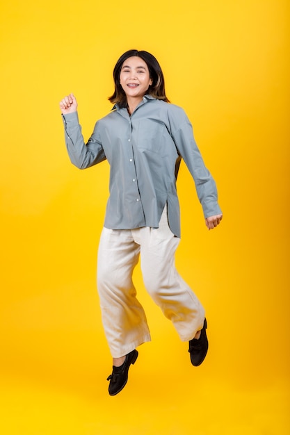 La animada joven asiática vestida con camisa y pantalones casuales de manga larga disfruta de un emocionante juego de divertidos saltos y bailes para estirarse y un ejercicio fácil para un espectáculo de refrigerios de salud en el retrato recortado
