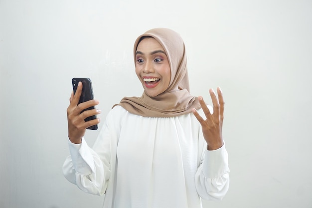 Animada linda mulher muçulmana asiática mostrando telefone celular isolado sobre fundo branco