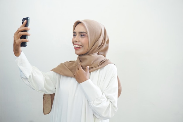 Animada linda mulher muçulmana asiática mostrando telefone celular isolado sobre fundo branco