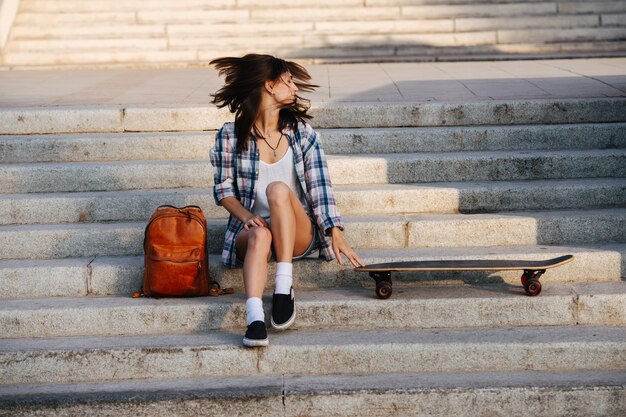 Animada mujer sentada en las escaleras junto a su patineta moviendo la cabeza