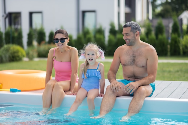 Foto animado antes de nadar. filha loira alegre e animada antes de nadar na piscina com os pais