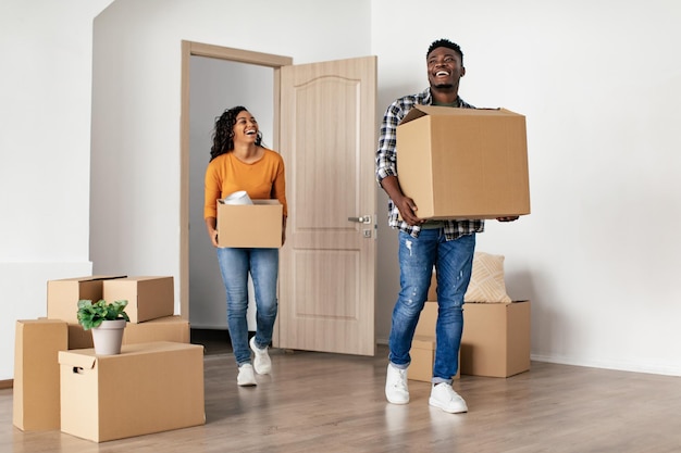 Animado casal africano carregando caixas de mudança olhando para casa nova