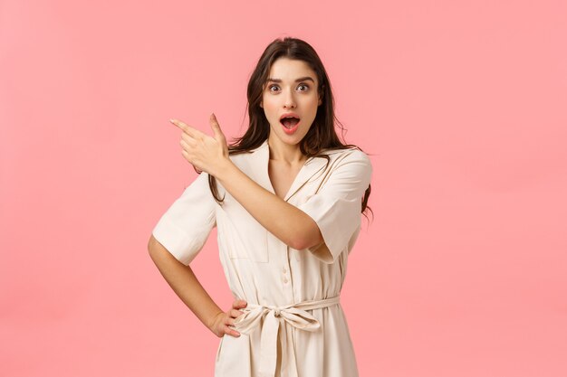 Animado e impressionado linda mulher caucasiana, mostrando grandes descontos de compras, preços promocionais nos feriados, se preparando para o dia das mães, escolhendo presentes, parede rosa de pé