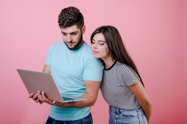 Animado feliz sorridente jovem casal homem e mulher, juntamente com o laptop isolado sobre rosa