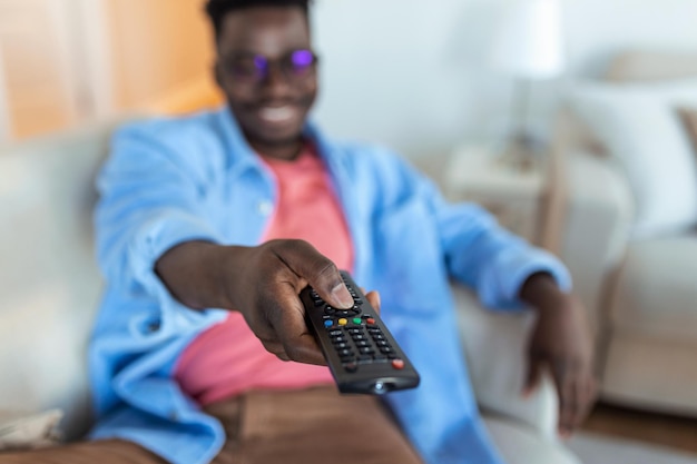 Animado homem afro-americano apontando o controlador de televisão para canais de comutação de câmera assistindo TV. Propaganda de Programação de Televisão. Foco Seletivo