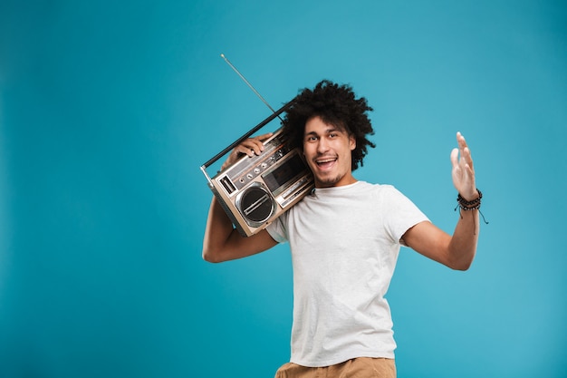 Animado jovem africano encaracolado segurando o boombox.