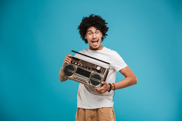 Animado jovem africano encaracolado segurando o boombox.