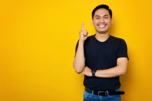 Animado jovem asiático em camiseta casual apontando o dedo para cima tendo uma ideia ou solução encontrada isolada em fundo amarelo Conceito de estilo de vida de pessoas