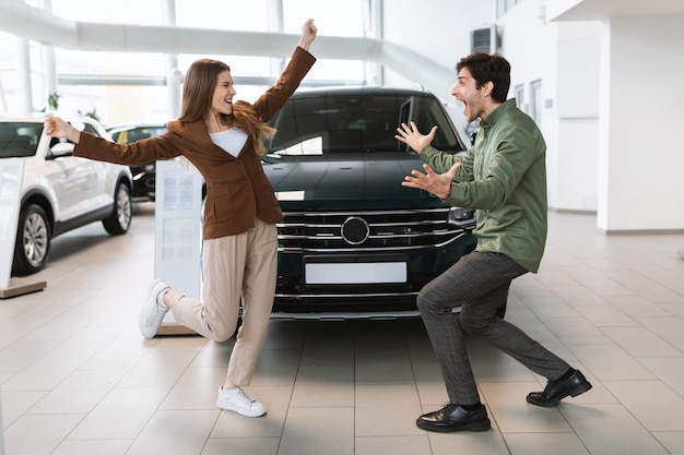 Animado jovem casal caucasiano comemorando a compra de carro bem-sucedida dançando e se divertindo no auto