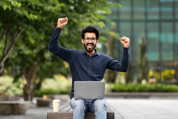 Animado jovem empresário do Oriente Médio comemorando sucesso usando laptop ao ar livre