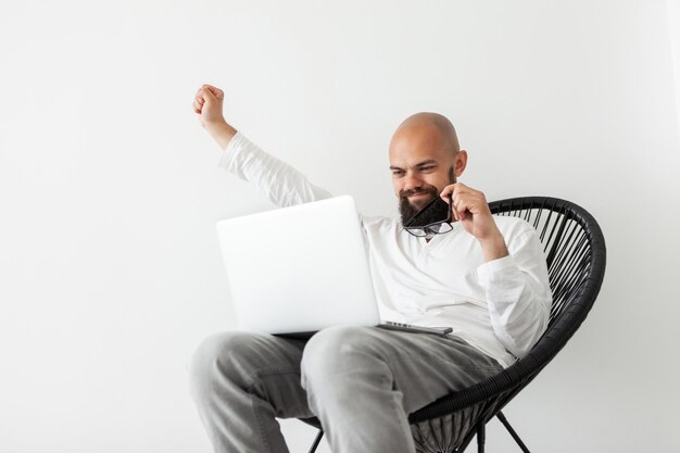 Animado jovem freelancer barbudo sortudo sentado na cadeira com o laptop levantou os punhos comemorando o sucesso fazendo sim o gesto foi promovido ganhou o conceito de vitória na loteria