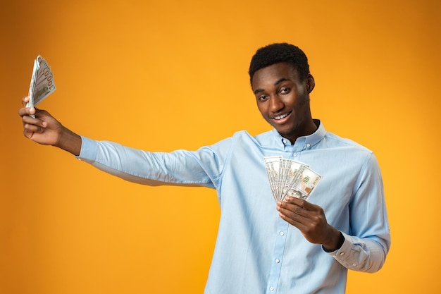 Animado negro segurando pilha de dólares no estúdio amarelo