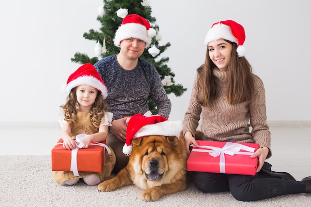 Animal de estimação, feriados e conceito festivo - família com cachorro está sentado no chão perto da árvore de Natal.