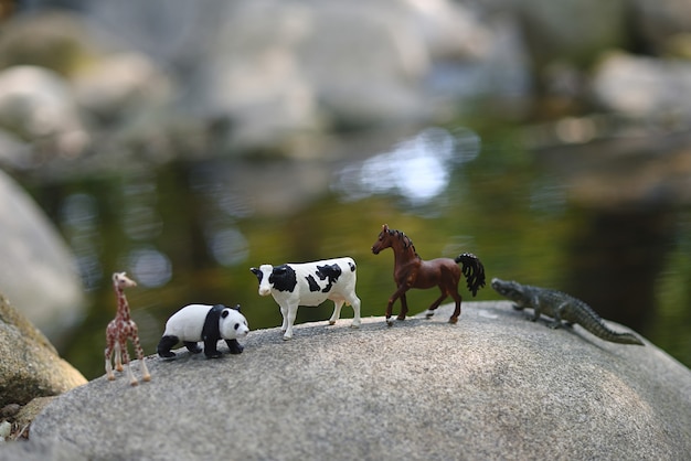 Animales de juguete en miniatura sobre rocas en el río.