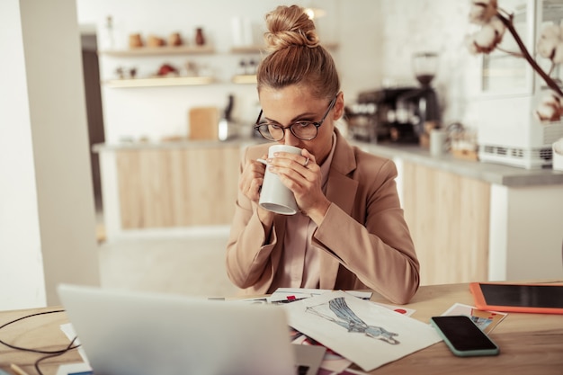 Animando-se. designer de moda concentrada olhando para o laptop e bebendo café sentado em seu local de trabalho.