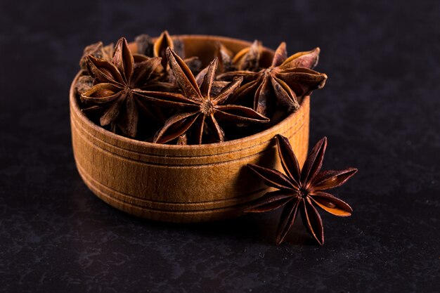 Anís estrellado en un recipiente de madera sobre una mesa negra. copyspace