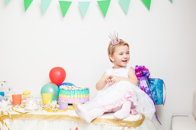 Aniversariante com coroa na cabeça segurando balões coloridos. A princesa menina na festa de aniversário