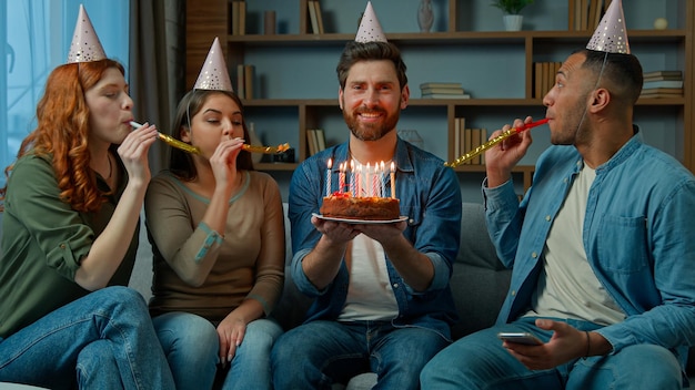 Aniversariante feliz adulto barbudo segura bolo festivo queimando velas diversos grupos de amigos