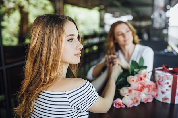 Aniversário da mamãe! filha apresenta um presente e um buquê de rosas em um café com terraço de verão