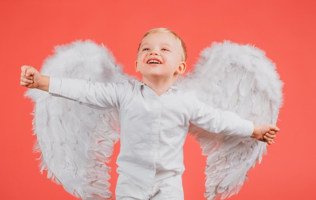 Anjo animado garotinho com asas brancas Menino de crianças angélicas feliz rindo Garoto bonito com asas brancas Cupido de criança adorável isolado em vermelho cartão de dia dos namorados baner cópia spase Cara engraçada