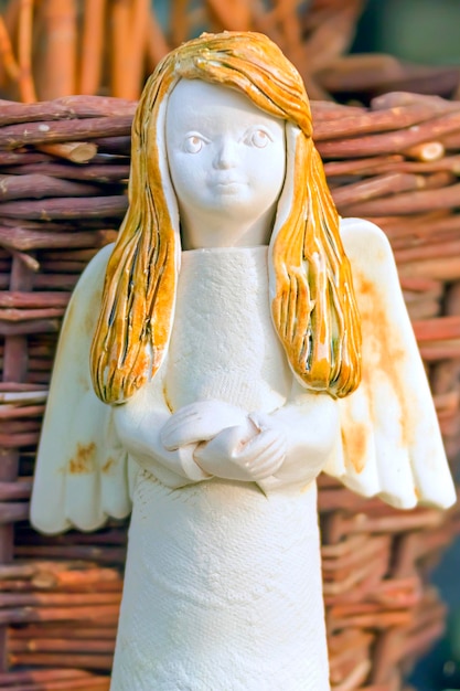 Anjo cerâmico branco com cabelo amarelo no fundo de uma cesta de vime