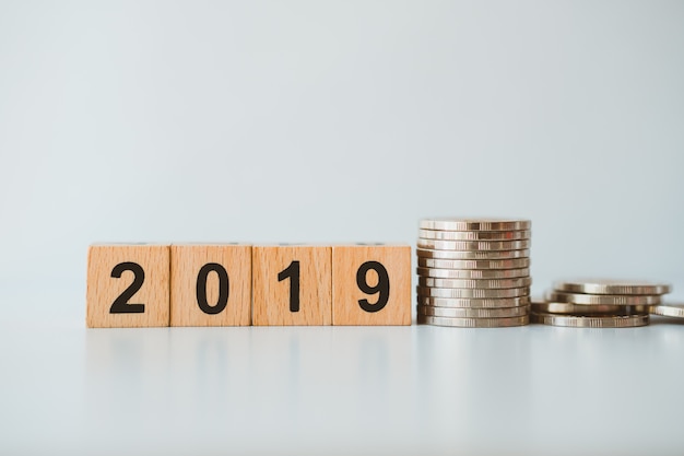 El año 2019 del bloque de madera con las monedas de la pila en fondo gris usando como concepto del negocio y de las finanzas