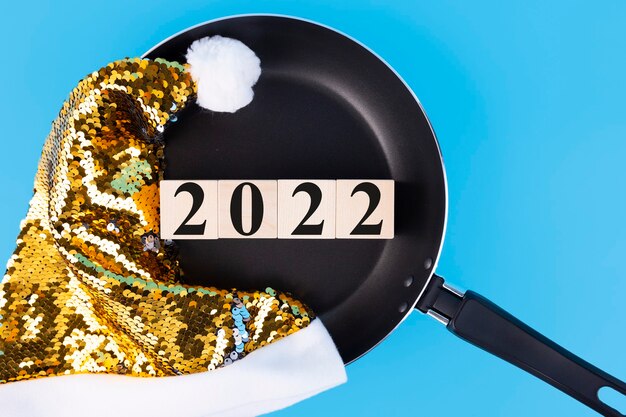 Foto año 2022, escrito en cubos de madera acostado en una sartén con un sombrero dorado de papá noel.