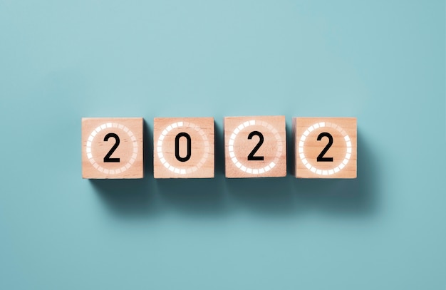 Año 2022 con signo de carga en bloque de cubo de madera con fondo azul, feliz Navidad y feliz año nuevo concepto de preparación.