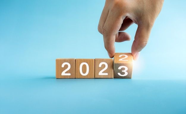 El año calendario 2022 cambió al concepto de éxito 2023 Bloques de cubos de madera girando a mano para la transición de 2022 a 2023 preparación para feliz Navidad y feliz año nuevo sobre fondo azul