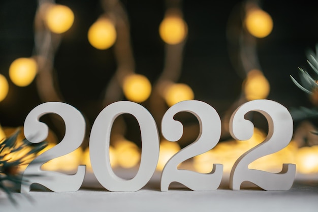 Foto ano novo 2022. números de madeira brancos 2022 estão com galhos de árvores de natal contra lâmpadas de guirlanda. copie o espaço