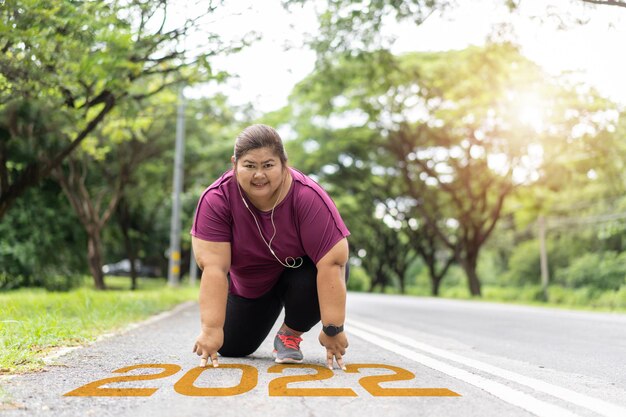 Ano novo 2022 ou comece o conceito em linha reta. Palavra 2022 escrita na estrada de asfalto e mulher gorda asiática pronta para perder peso