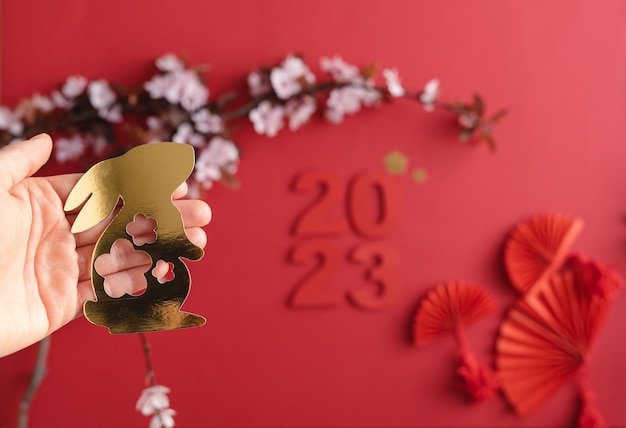 Ano novo chinês do coelho Fundo vermelho com coelho dourado em papel cortado em uma decoração de ramo de ameixa de mão mujecon com flores e fãs