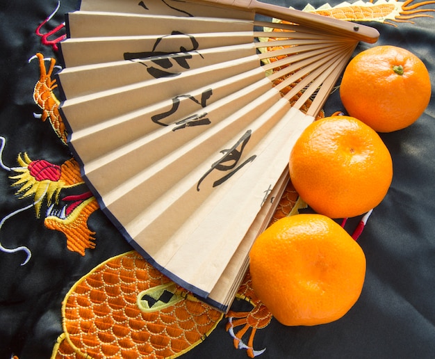 Ano novo chinês, tangerinas e um fã deitado sobre o tecido de seda com um dragão bordado