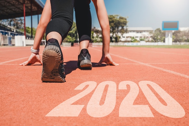 Ano novo de 2020, atleta mulher que começa em linha para um começo correndo com o número 2020 comece para ano novo.