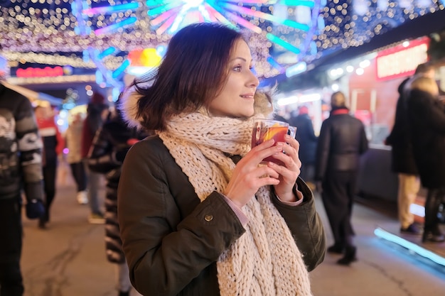 Ano Novo, Natal, mercado noturno festivo da cidade, mulher madura e feliz com uma caneca de vinho quente