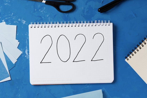 Foto año nuevo 2022 en el bloc de notas y accesorios sobre fondo azul. celebración de oficina