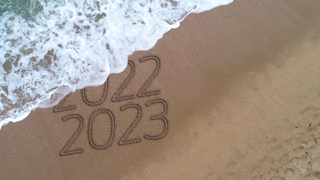 Año nuevo 2023 escrito a mano en la superficie de la arena.