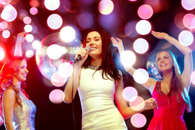 año nuevo, celebración, amigos, despedida de soltera, concepto de cumpleaños - tres mujeres vestidas de noche bailando y cantando karaoke