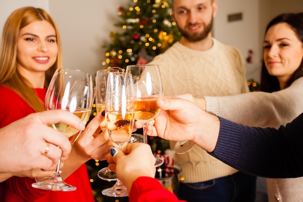 Año nuevo o fiesta de Navidad en casa, hermanos y hermanas animando deseándose lo mejor el uno al otro. Cerrar vista de manos de jóvenes tintineo copas de champán juntos