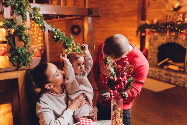 Año Nuevo o Navidad, retrato de una hermosa familia, padre, madre e hija cerca del árbol de Año Nuevo, noche de Navidad, una familia tierna y feliz en invierno, el padre sostiene a su hija en sus brazos.