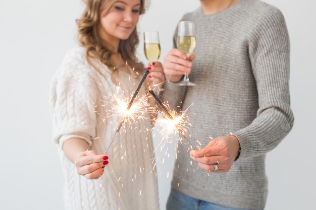 Año nuevo pareja amorosa sosteniendo luces de bengala y copas de champán sobre la pared blanca de cerca