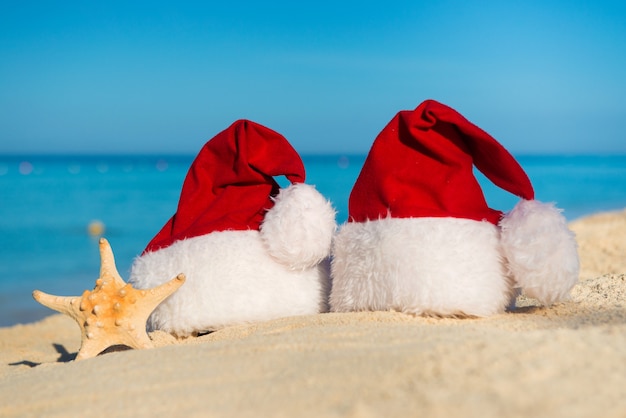 Año nuevo romántico en el mar. Vacaciones de Navidad. Sombreros de Santa en la playa de arena