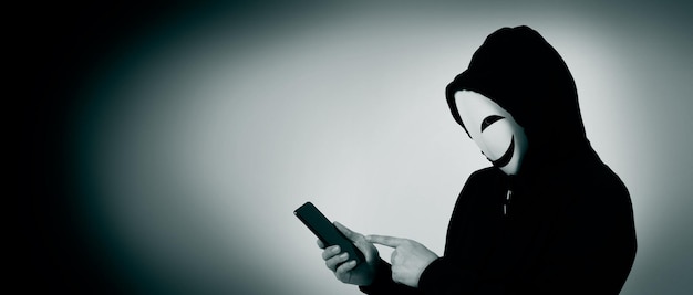 Anonymer Hacker und Gesichtsmaske mit Smartphone in der Hand