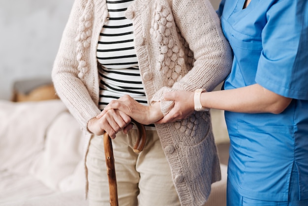 Foto anos de ocaso. admirável trabalhador da área médica certificando-se de que a senhora idosa fica de pé firme enquanto tenta dar um passeio em casa